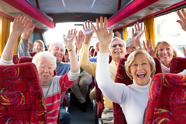 group of elderly people with their arms raised having a good time in a tour bus