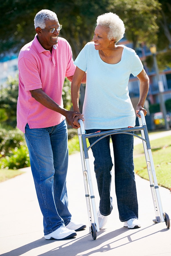 senior man ehlping senior woman walk with a walker