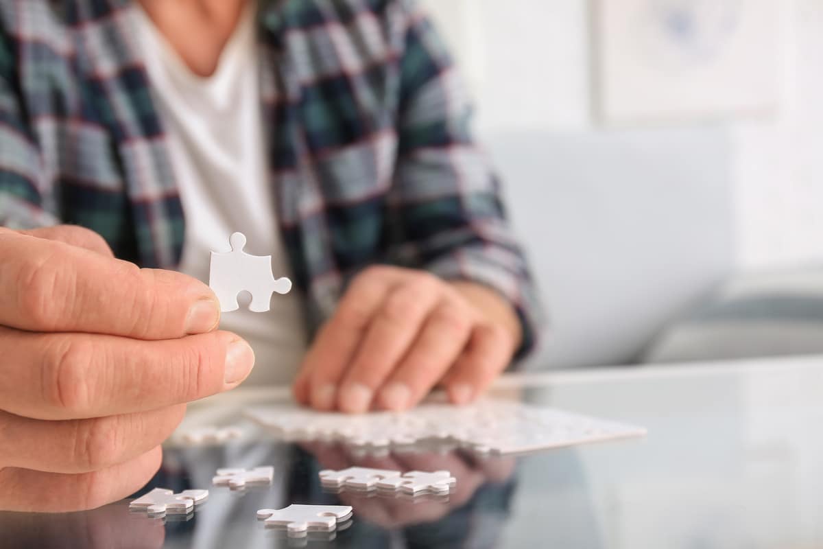 Senior man with Parkinson syndrome doing puzzle at home, closeup