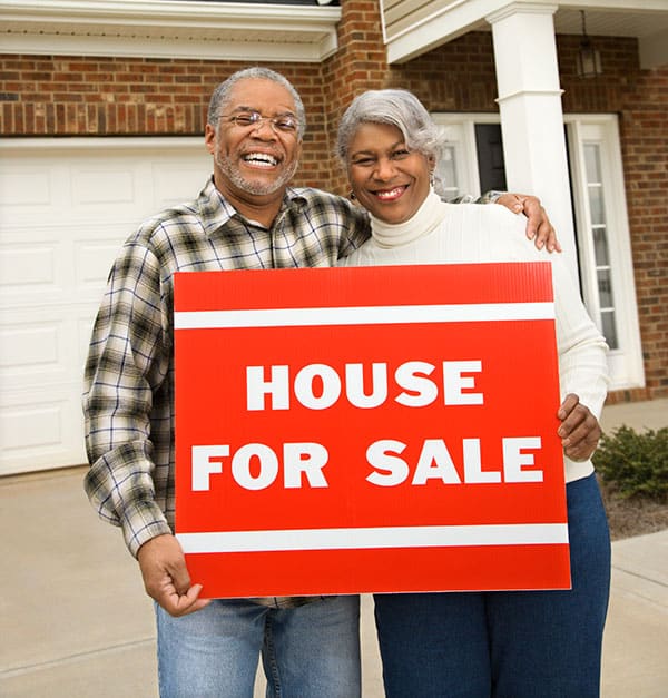 Senior couple holding a for sale sign in front of house
