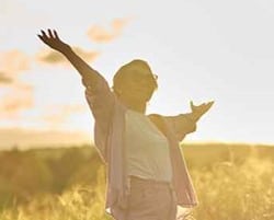 Senior woman in fields with arms spread out.