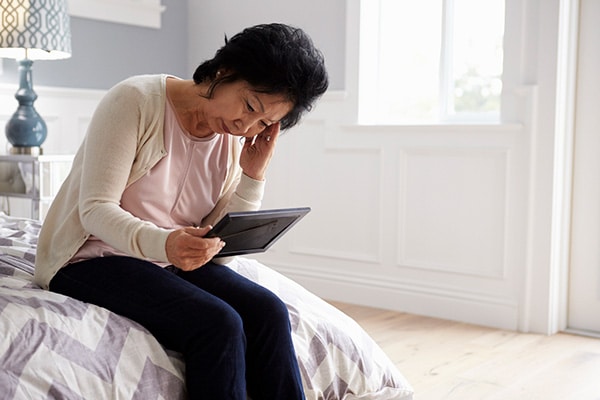 senior woman sitting on a bed looking at an ipad