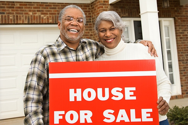 Senior Couple with House for Sale sign