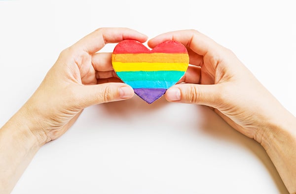 hand holding LGBTQ rainbow colored heart shape