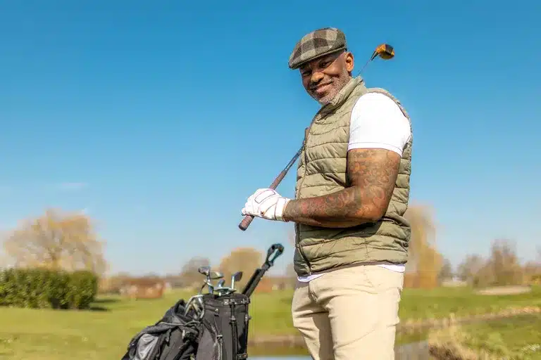 senior man playing gold and smiling at the camera