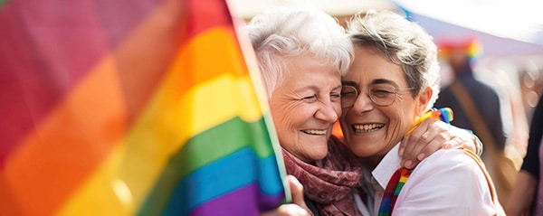 senior ladies hugging while holding Pride flag